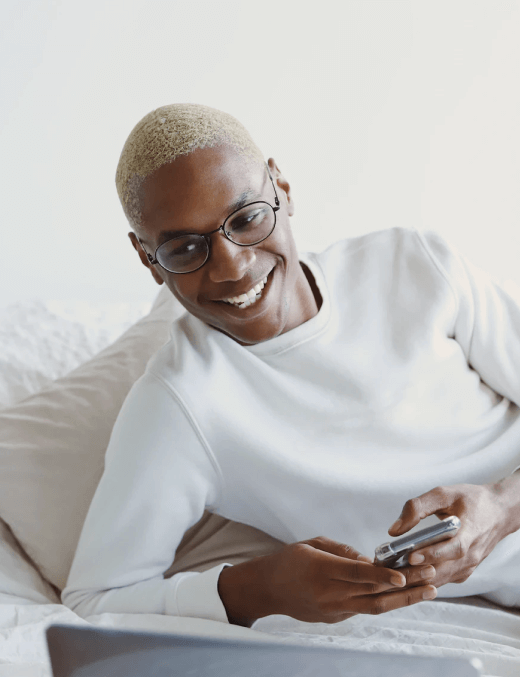 A Young Stylish Man Smiling Whilst Using A Laptop and Smartphone